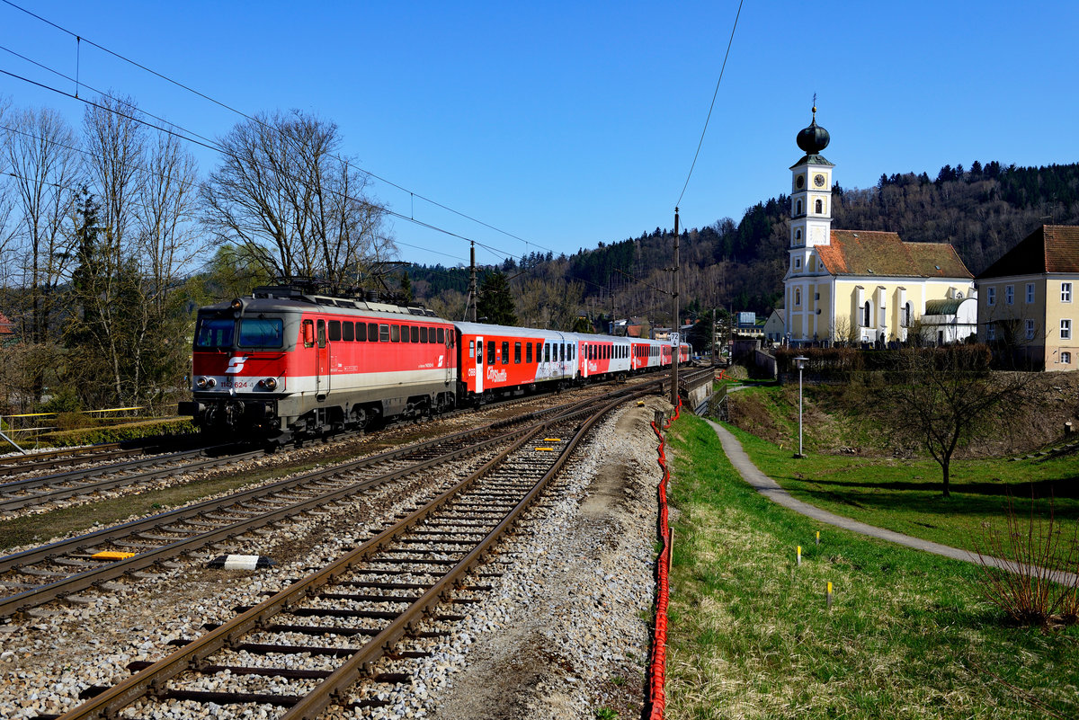 Bald wird es mit dieser idyllischen Szenerie vorbei sein: Der Bahnhof Wernstein wird in absehbarer Zeit komplett umgebaut und Lärmschutzwände werden errichtet.  Am 08. April 2018 war die Welt aus Fotografensicht noch halbwegs in Ordnung, zumal der R 5917 nach Neumarkt-Kallham an diesem Tag aus 1142.624 und einer CityShuttle Garnitur gebildet wurde. Interessanterweise wurde die Lok wohl in jüngerer Vergangenheit nachträglich mit einem  Pflatsch  versehen. 