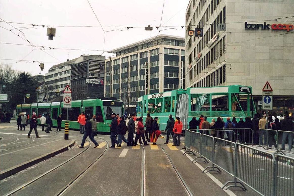 Basel Fasnacht 2005_Das gabs nur einmal: ein 'Combino'-Tram kommt am Aeschenplatz aus der Dufourstraße und biegt in die Aeschenvorstadt ein. Parallelfahrt zweier Combinos verschiedener Bauart ! Nachdem Siemens 2004 wegen konzeptioneller Mängel an den Wagenkästen schlagartig sämtliche (ca. 450) Combinos weltweit aus Sicherheitsgründen stilllegen lassen mußte, zeigten Basler Fasnachter der 'Loge-Clique' ihre Alternativ-Konstruktion. Nach Überarbeitung haben sich aber die Siemens Combinos bis heute als die stabileren erwiesen.