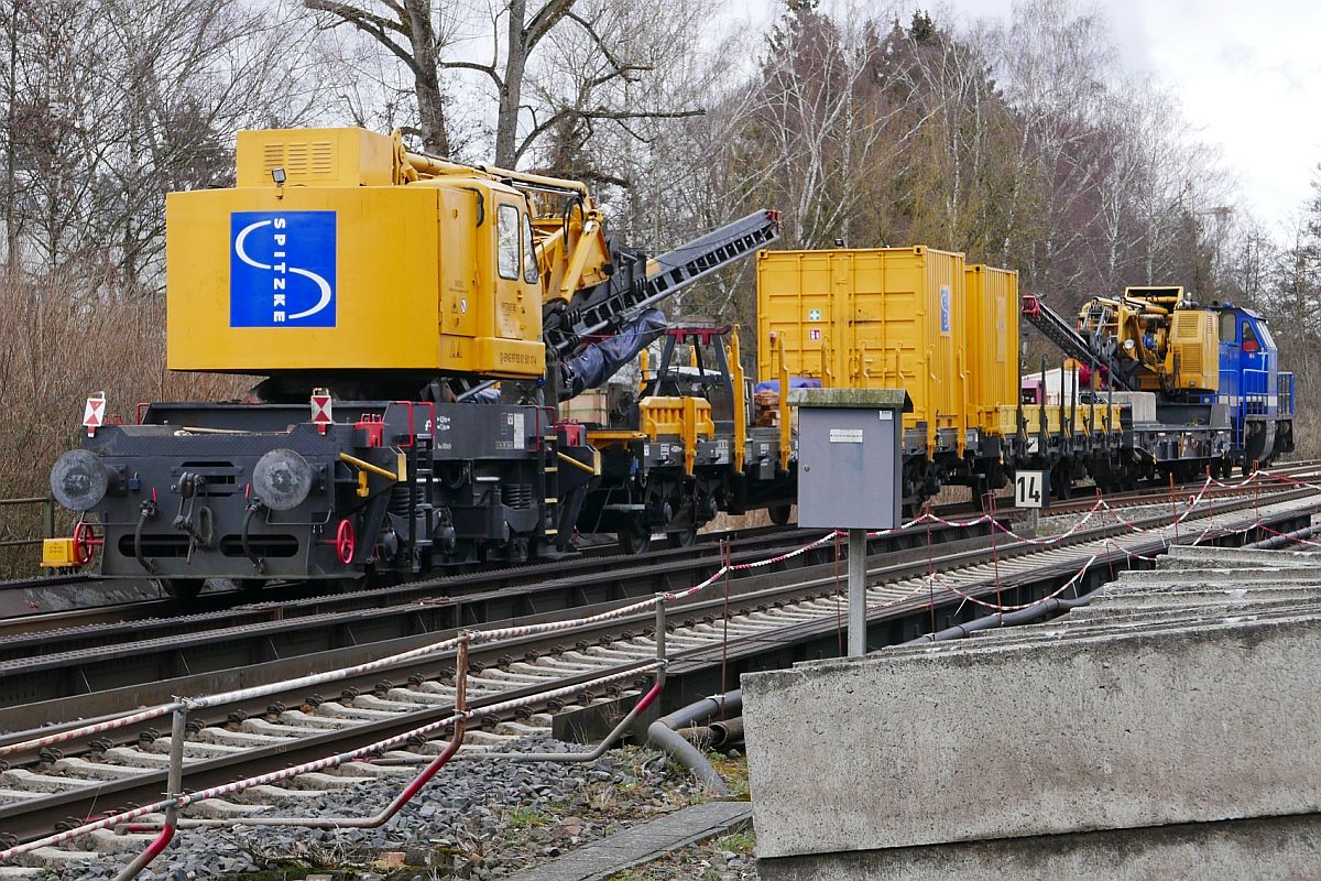 Bauarbeiten zur Elektrifizierung der Südbahn, Streckenabschnitt Biberach - Aulendorf. V100-SP-027 der SLG SPITZKE LOGISTIK GmbH steht am 11.03.2019 mit zwei gleisgebundenen Rammen und zwei Flachwagen zwischen dem Bahnhof Biberach (Riß) und der Haltestelle Biberach Süd.