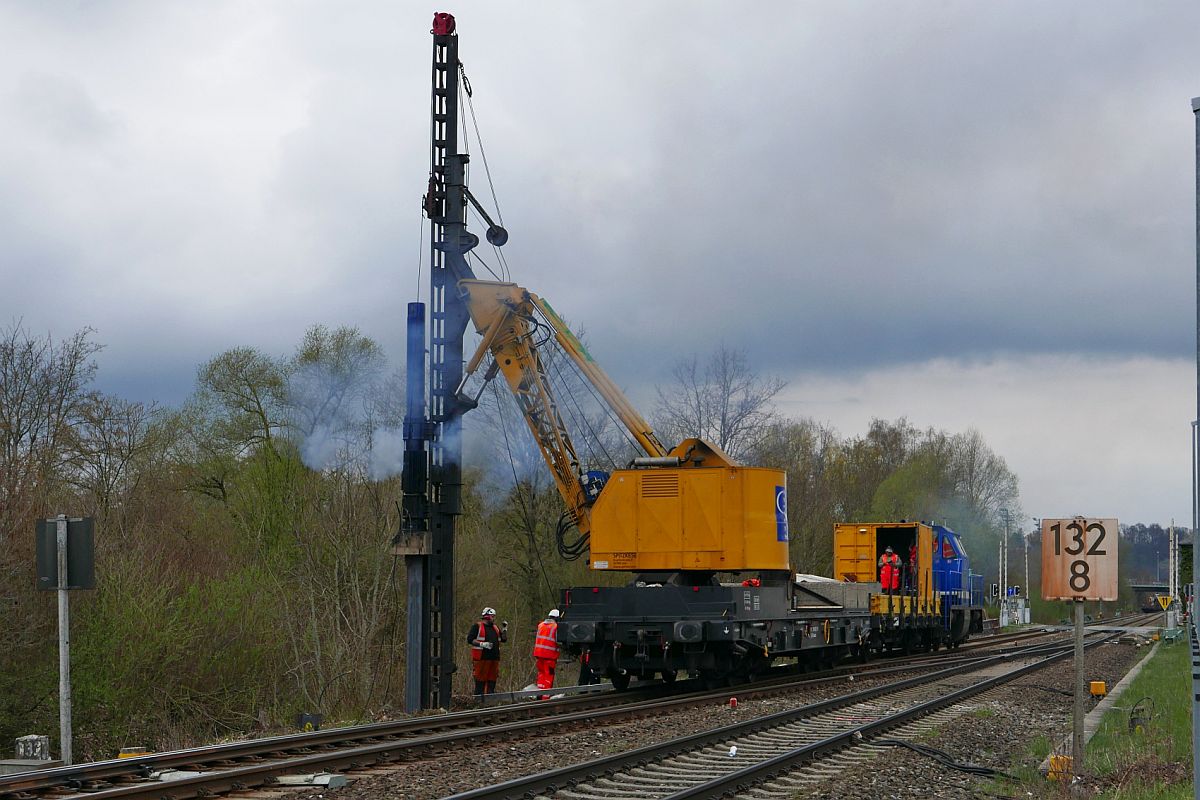 Bauarbeiten zur Elektrifizierung der Südbahn, Streckenabschnitt Biberach - Aulendorf. In Verbindung mit dem Fundament für einen Oberleitungsmasten treibt die auf einem Drehgestellflachwagen der Gattung Samms (81 80 4865 384-9) befindliche Ramme von SPITZKE in der Nähe der Haltestelle Biberach Süd einen zwischen 6,5 m und 8 m langen Doppel-T-Träger in den Boden (08.04.2019).