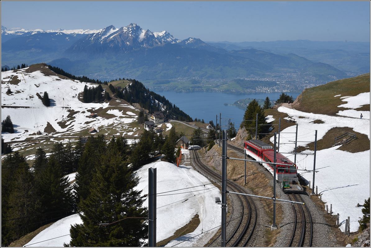 BDhe 4/4 22 + Bt verlassen Rigi Kulm Richtung Vitznau. Im Hintergrund Luzern, Vierwaldstättersee und Pilatus 2128m. (20.04.2018)
