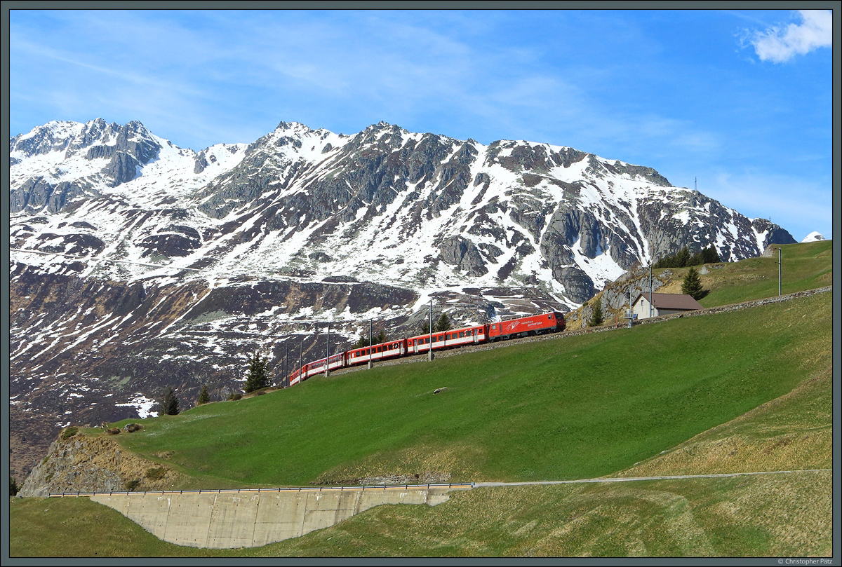 Bei Andermatt windet sich die Oberalppassstrecke in mehreren Schleifen am Hang des Nätschen nach oben. Am 19.04.2022 zieht HGe 4/4 II Nr. 1 einen Personenzug Richtung Sedrun. Im Hintergrund ist der Spitziggrad zu sehen.