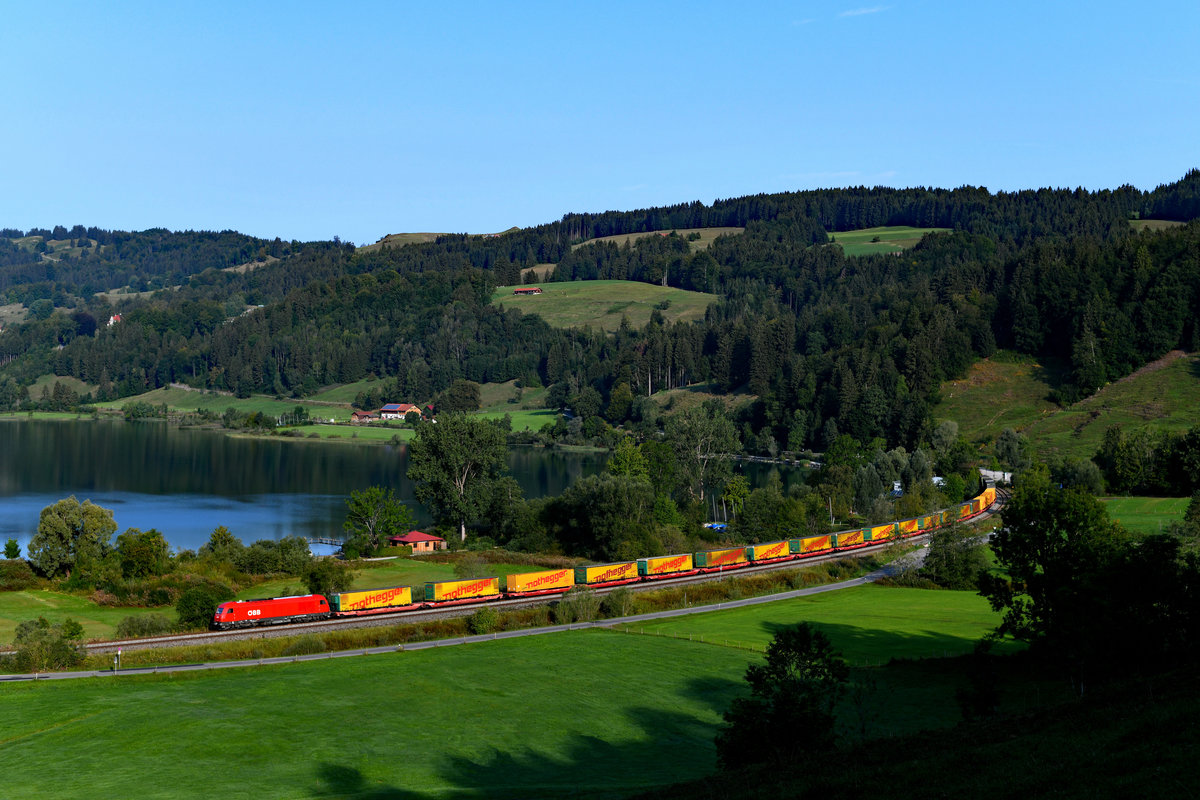 Bei der diesjährigen Arlberg-Sperre konnten interessanterweise auch private Güterzüge und Züge unter ÖBB-Regie beobachtet werden. Am 28. August 2018 war es mir vergönnt, eine dieser Leistungen fotografieren zu können. Der DGS 43193 von Dietlikon in der Schweiz nach Wels ist einheitlich mit Aufliegern der Spedition Nothegger beladen und dadurch sehr fotogen. An diesem Tage wies er eine beträchtliche Verspätung auf und konnte daher bei Hub mit Blick auf den Alpsee dokumentiert werden. Der in Deutschland unter der Zugnummer DGS 52628 verkehrende Zug wurde von der kürzlich mit Neulack versehenen 2016.041 befördert. 