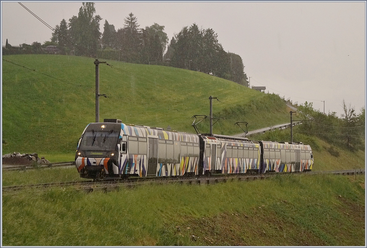 Bei einem starken Regenschauer ist der MOB Be 4/4 5001 mit seinen Steuerwagen ABt 341 und Bt 241 als Regionalzug 2238 bei Planchamp auf dem Weg von Montreux nach Zweisimmen. 
Der Zug wurde von Sarah Morris in dieser gelungen Form als  Monarch  gestaltet. 

26. April 2020
