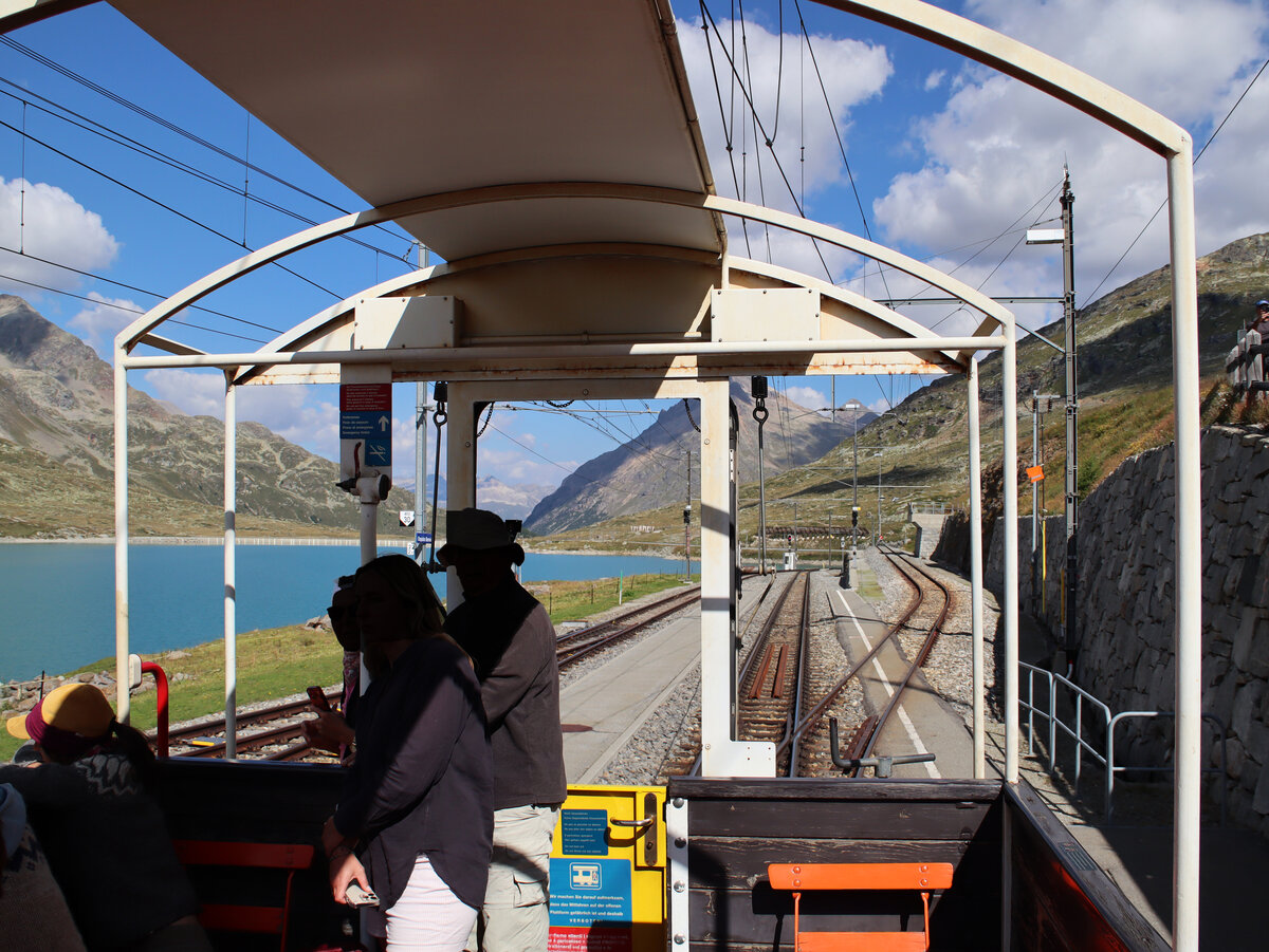 Bei einigen Regionalzügen zwischen St. Moritz und Tirano über die Berninastrecke rollen in den Monaten Juli und August offene Panoramawagen mit, ein spezielles Vergnügen in der frischen Bergluft. Diese Aufnahme entstand im Bahnhof Ospizio Bernina (2253 Meter über Meer). Links der Lago Bianco, an dessen Ende im Hintergrund befindet sich die Wasserscheide Adriatiches / Schwarzes Meer. Ospizio Bernina, 21.8.2023