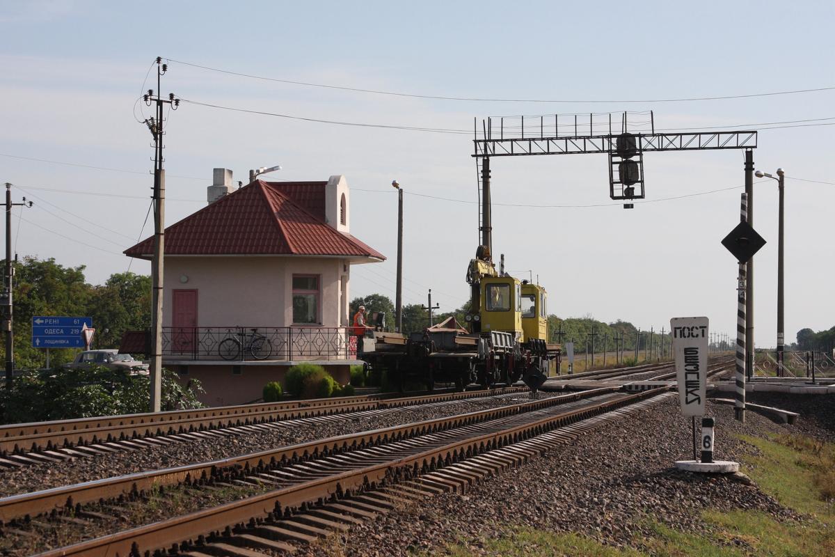 Bei Ismajil war am 3.9.2009 ein kleiner Schienenkran unterwegs. Er passiert hier gerade einen mit Schrankenwärter gesicherten Bahnübergang. Man beachte die Sauberkeit rundum. Ich habe durchweg, teilweise auch mit viel Blumenschmuck,  gepflegte Bahnwärterhäuser gesehen. 