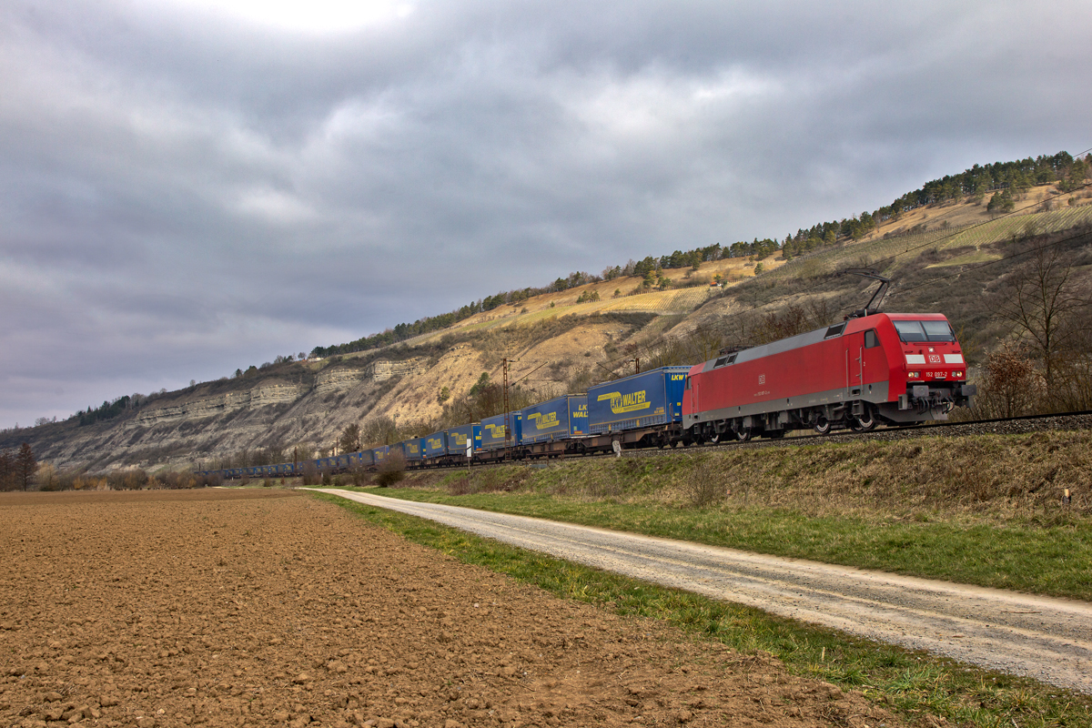 Bei starkem Ostwind fährt am Morgen des 13.3.2016 in Thüngersheim die 152 097-2 mit einem LKW Walter Zug vorüber.