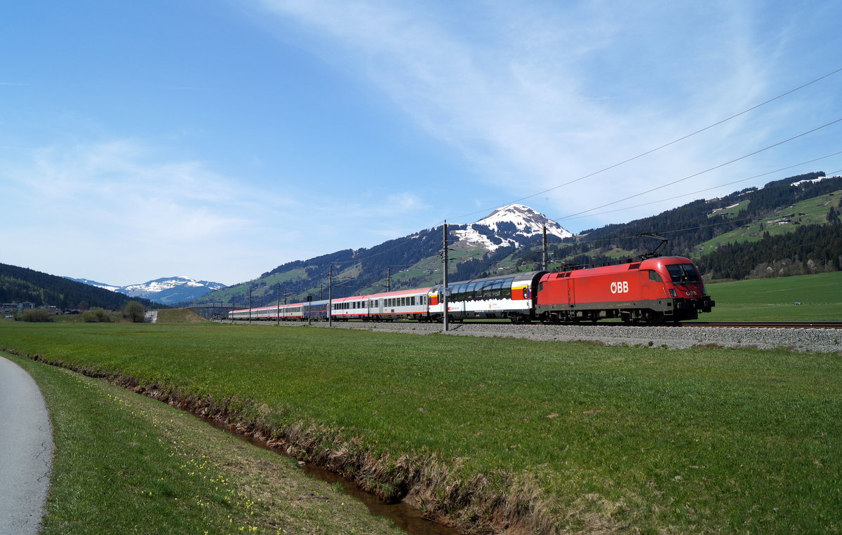 Bei vorfrühlingshafter Stimmung ist der Plan-Paradezug der Salzburg-Tiroler-Bahn, der Eurocity  Transalpin  (163), auf seinem Weg von Zürich HB nach Graz Hbf nahe Brixen im Thale unterwegs und wird in wenigen Minuten gering verspätet den Bahnhof Kirchberg in Tirol erreichen, 22.04.2019.