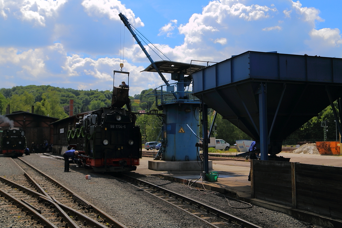 Bekohlung a la Weißeritztalbahn, hier veranschaulicht an 99 1734 am 17.06.2017 im Bw Freital-Hainsberg, während der Eröffnungsveranstaltung für den wiederaufgebauten Streckenabschnitt Dippoldiswalde - Kurort Kipsdorf. Die für die Loks benötigte Steinkohle wird mittels Bagger aus dem Kohlebansen in den rechts zu sehenden Beschickungsbunker gefördert. Aus diesem wird der Brennstoff in den darunter befindlichen  Japaner  dosiert, welcher dann mittels Kran über den Kohlekasten der Lok gehoben wird. Hier braucht er dann vom Lokpersonal nur noch durch Kippen entleert zu werden. Immer wieder herrlich, diesem wahrhaft bahnnostalgischen Vorgang zuschauen zu können!