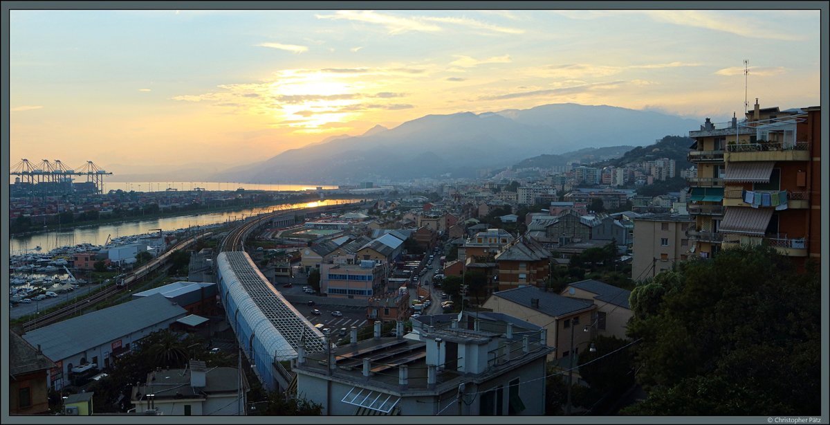 Beleuchtet vom Licht der langsam untergehenden Sonne zieht am 21.09.2018 eine E.402 den IC 681 Ventimiglia - Mailand durch die Hafenanlagen am Bahnhof Genova Pra. In Krze wird der Bahnhof Genova Piazza Principe erreicht. Der beeindruckende Panoramablick bot sich aus dem Hotelzimmer in Genova-Pegli. 