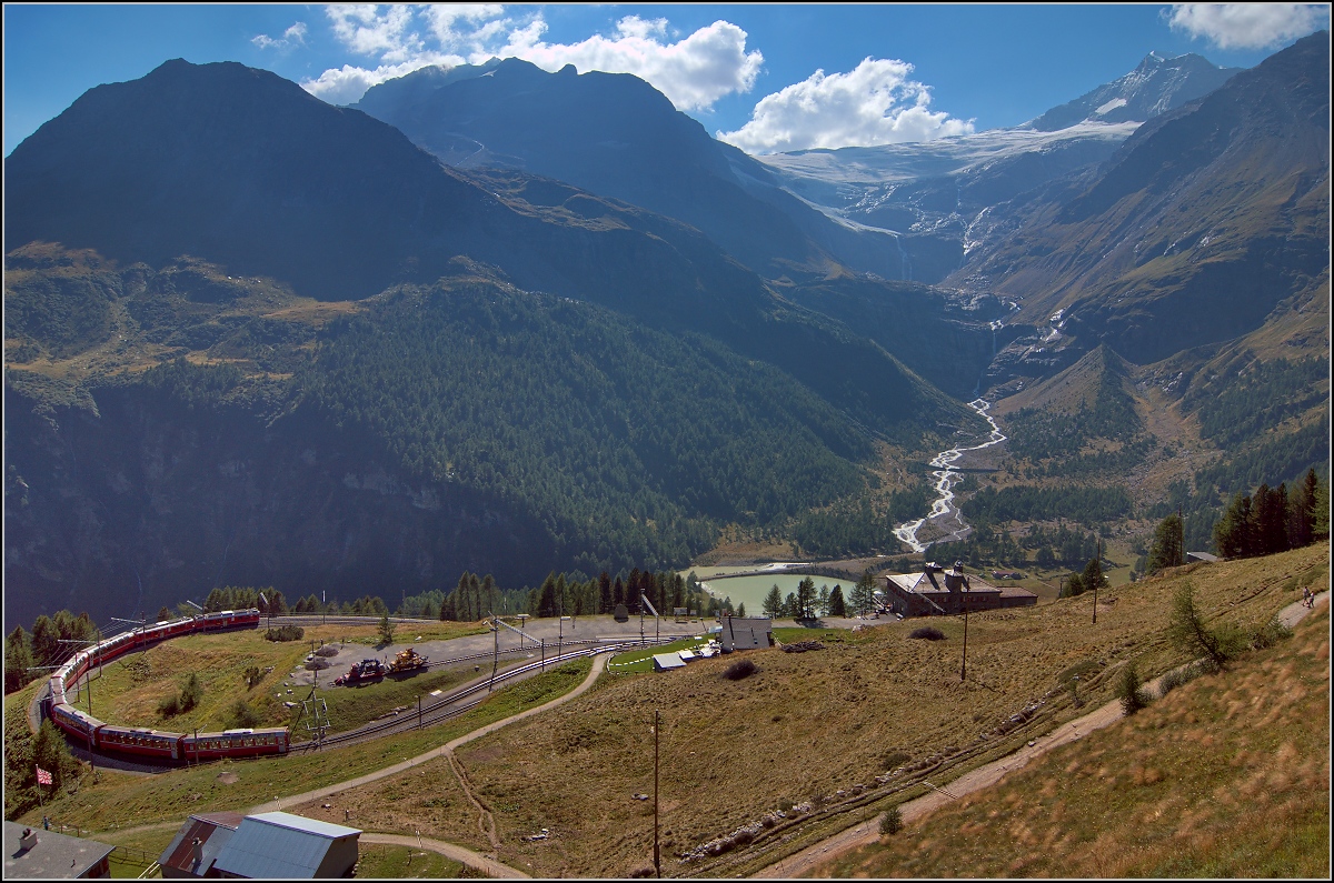 Berninaexpress Richtung Tirano mit zwei ABe 4/4 <sup>III</sup> in der bekannte Kehre auf der Alp Grüm, höchstwahrscheinlich Nr. 52 Brusio und Nr. 54 Hakone. Im Hintergrund der markant breite Palügletscher, der sich mit gut 600 Höhenmetern inzwischen besonders deutlich zurückgezogen hat. Rechts ist der Piz Palü mit 3900 m sehen. August 2015. Hier würde sich wohl ein morgendlicher Aufnahmezeitpunkt empfehlen, sozusagen auf dem Hinweg, aber eindrücklich ist die Szene auch im Gegenlicht.