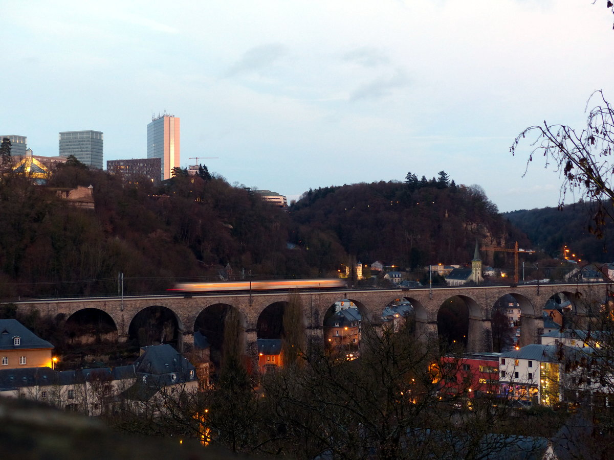 Bewegungsunschärfe. In der Abendsonne des 26.12.2016 rauschte ein Zug der Reihe 2000 über das Pfaffenthal-Viadukt. Die Lichter der Stadt Luxemburg werden derweil nach und nach eingeschaltet.