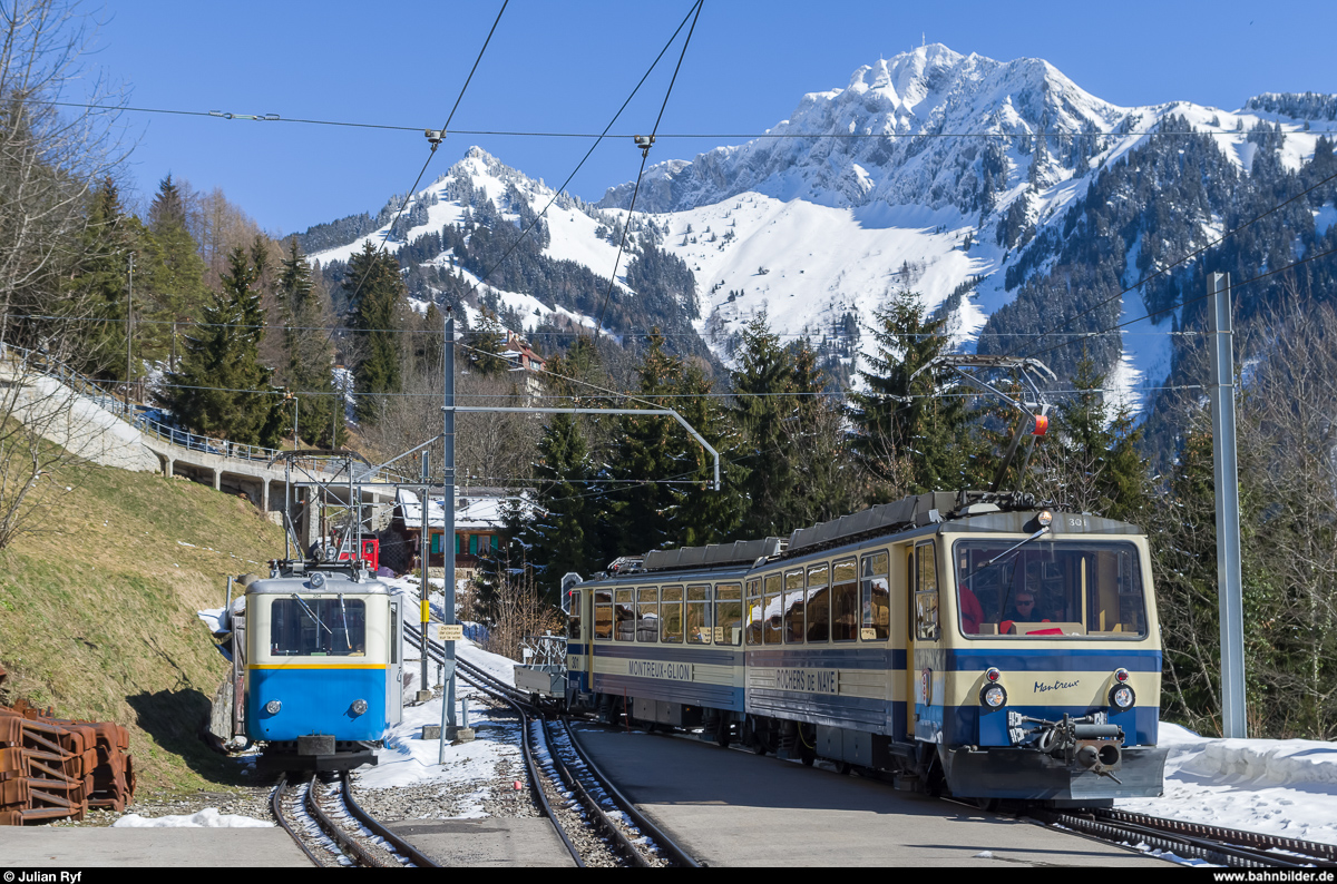 Bhe 2/4 204 ist vor kurzem von seinem Schülerzug aus Haut-de-Caux in den Bahnhof Caux zurückgekommen und steht nun auf dem Abstellgleis um Platz für die Kreuzung der beiden Regelzüge zu machen. Danach wird er wieder nach Haut-de-Caux fahren um die Schüler nach dem Mittag wieder nach Montreux hinunter zu bringen. Dem talwärts fahrenden Bhe 4/8 301 folgt  die eine der beiden neuen Stadler Lokomotiven, Hem 2/2 12, die gerade von der Schneeräumung mit der neuen Zaugg Schneefräse zurückkommt. Über der Szene ist der Gipfel des Rochers de Naye zu sehen.
Aufgenommen am 6. März 2015.