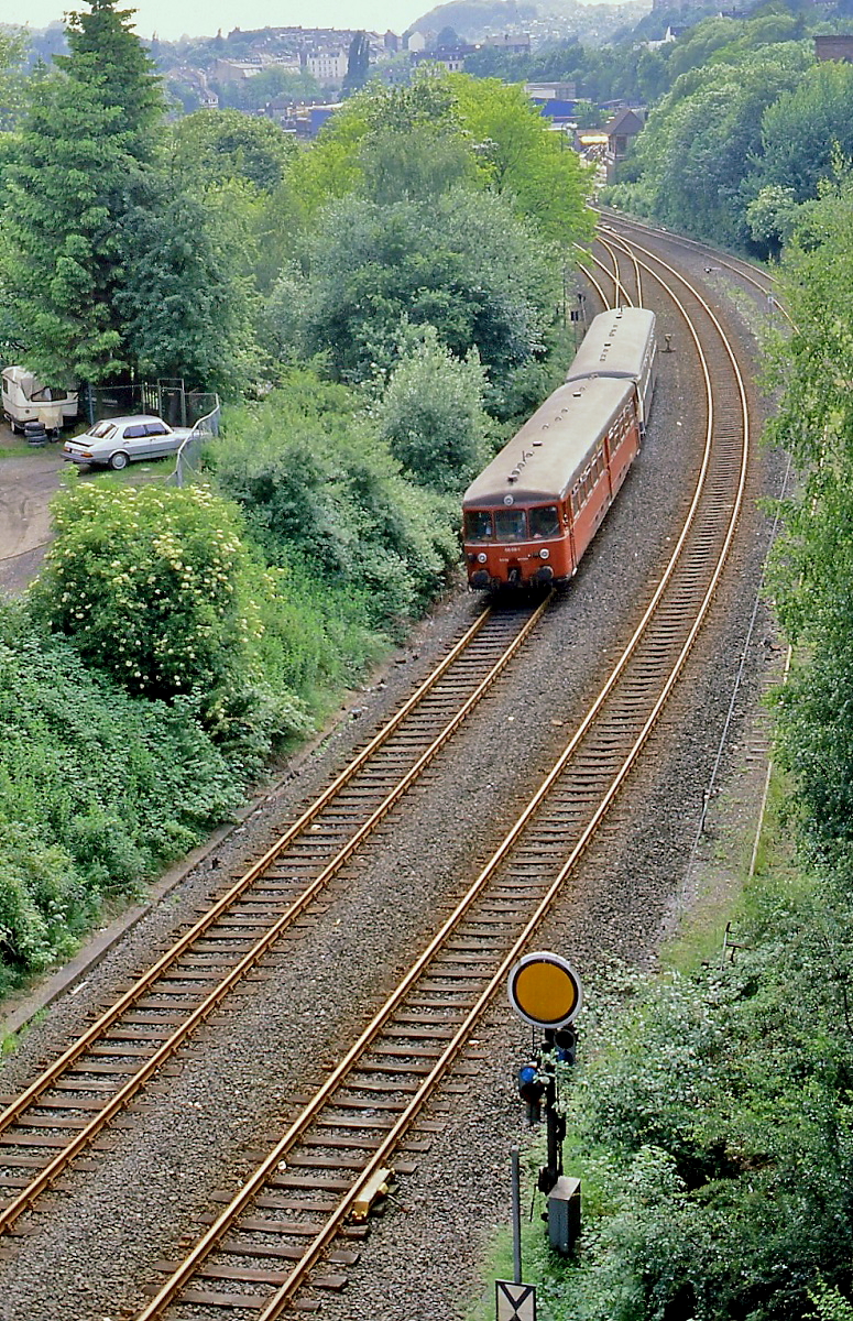 Bis zur Einstellung im Jahre 1991 verkehrten auf der Wuppertaler Nordbahn noch ein morgendliches und vorabendliches  Alibizugpaar  zwischen Düsseldorf Hauptbahnhof und Wuppertal Wichlinghausen, hier ist ein roter 515 mit einem beige-türkis lackiertem 815 Ende der 1980er Jahre zwischen Wuppertal-Ostersbaum und Wuppertal-Loh unterwegs. Während auf den Schienen der Rheinischen Strecke jetzt Radfahrer unterwegs sind, liegt das rechts sichtbare frühere Anschlussgleis zum Industriegebiet Clausen noch, heute ist man hier mit Draisinen unterwegs.