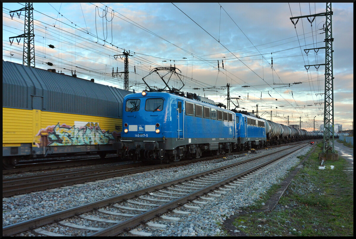Blaue Stunde: PRESS 140 017 & 037 mit einem Kesselwagenganzzug am 20.11.2023 in Würzburg. In Gegenrichtung passiert soeben die ebenfalls blaue Delta Rail 192 024 mit den ARS-Autotransportwagen die PRESS-Maschinen.