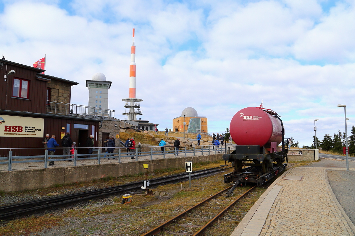Blick am Vormittag des 19.10.2018 in den Endbereich des Bahnhofes Brocken. Zwischen Bahnhofsgebäude und Kesselwagen sind die bis ins Tal sichtbaren Gipfelgebäude des Brockens zu sehen (von links: Aussichtsturm, Großsendemast, und Brockenmuseum).