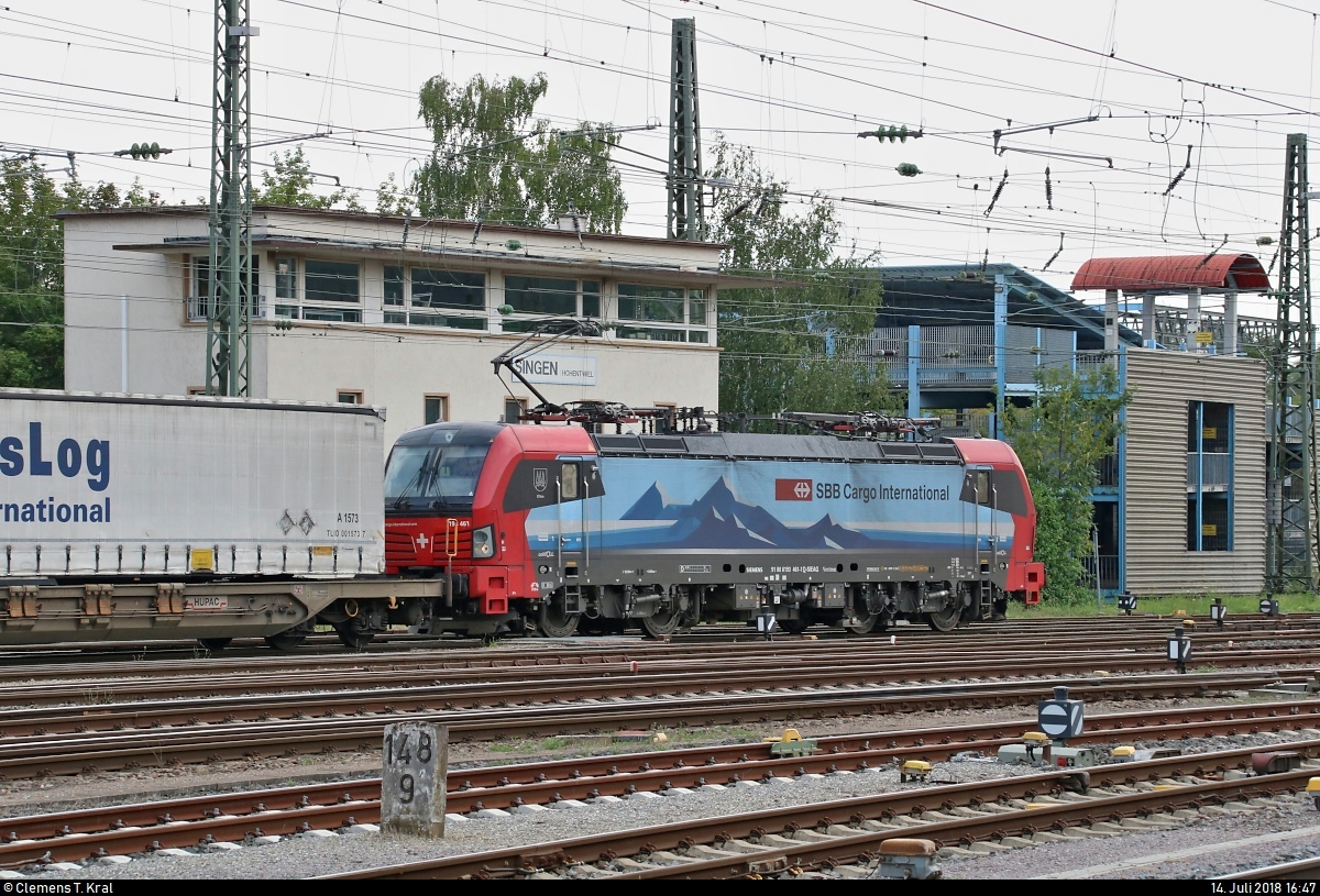 Blick auf 193 461-1  Olten  (Siemens Vectron) der SBB Cargo International mit Sattelaufliegern auf Flachwagen (KLV-Zug), die den Bahnhof Singen(Hohentwiel) in westlicher Richtung vor dem elektromechanischen Stellwerk Sf des Fahrdienstleiters (Fdl) verlässt.
Aufgenommen am Ende des Bahnsteigs 1.
[14.7.2018 | 16:47 Uhr]