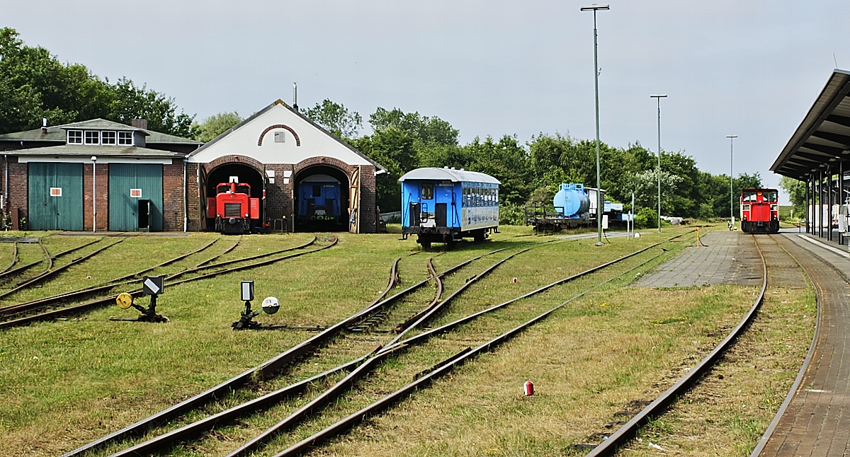 Blick auf die Anlagen des Wangerooger Ortsbahnhofes am 27.06.2018, links der Lokschuppen mit der von Faur/Rumänien gebaute 399 105-6, rechts am Hausbahnsteig eine der beiden Schoema-Loks