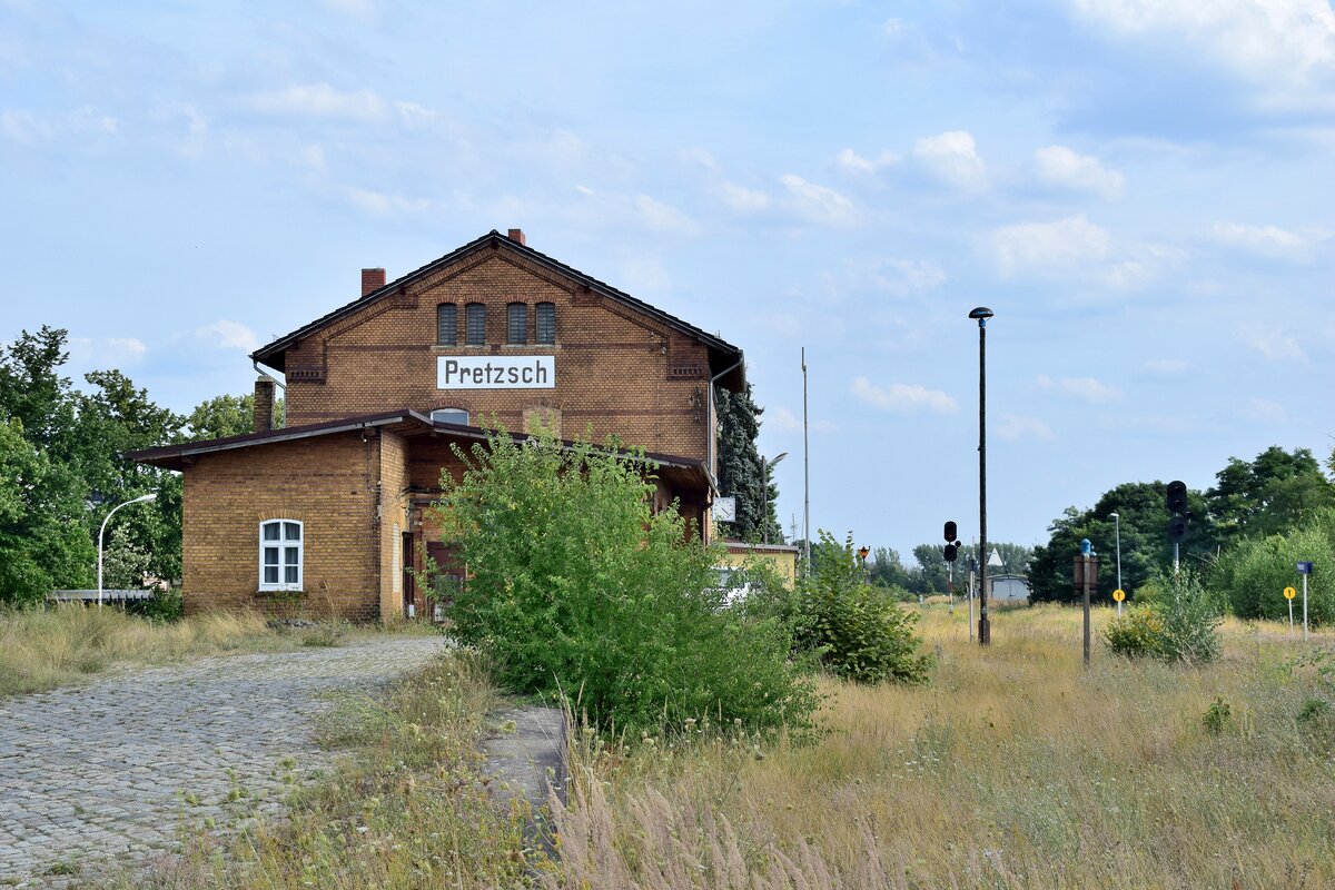 Blick auf die Laderampe, Empfangsgebäude und das verwilderte Gleisfeld in Pretzsch. Die EZMG Signale leuchten bis heute und hauchen dem Bahnhof so zumindest etwas Leben ein auch wenn hier seit Ende 2019 kein Zug mehr fahren darf. 1998 wurden die durchgehenden Züge nach Eilenburg eingestellt und der letzte Ast von Wittenberg nach Bad Schmiedeberg Ende 2014 eingestellt. Zuletzt gab es hier 2017 Sonderzüge. Ende 2019 wurde die Strecke wegen Oberbaumängeln betrieblich gesperrt. Seitdem verwildern einige Teile der Strecke zusehens.

Pretzsch 13.08.2021