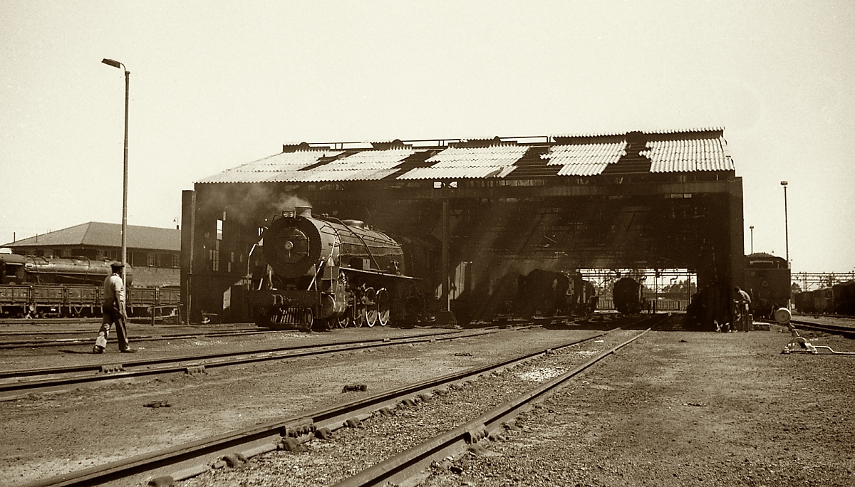Blick auf den Lokschuppen von Witbank (seit 2006 eMalahleni) in Transvaal mit einer Lokomotive der Class 15CA (November 1976). 84 dieser Lokomotiven wurden 1929/30 von verschiedenen Herstellern (Alco, Baldwin North British und Breda) geliefert. In Kohlerevier von Witbank wurden sie vor allem im schweren Güterzugdienst eingesetzt.