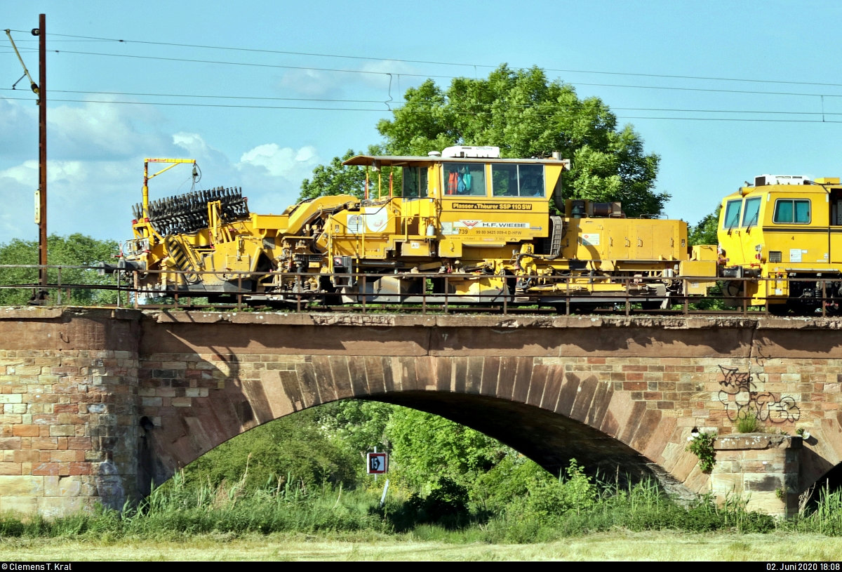 Blick auf die Schotterplanier- und Profilierungsmaschine Plasser & Theurer SSP 110 SW (Nr. 739 | 99 80 9425 009-4 D-HFW) der Wiebe Holding GmbH & Co. KG, die zusammen mit der unternehmenseigenen Universal-Gleisstopfmaschine Plasser & Theurer UNIMAT 09-32 4S  Bremen  (99 80 9124 007-2 D-HFW) und Zuglok 212 192-9 (V 100 2192 | DB V 100.20) die Saaleaue bei Angersdorf auf der Bahnstrecke Halle–Hann. Münden (KBS 590) Richtung Halle (Saale) überquert.
[2.6.2020 | 18:08 Uhr]