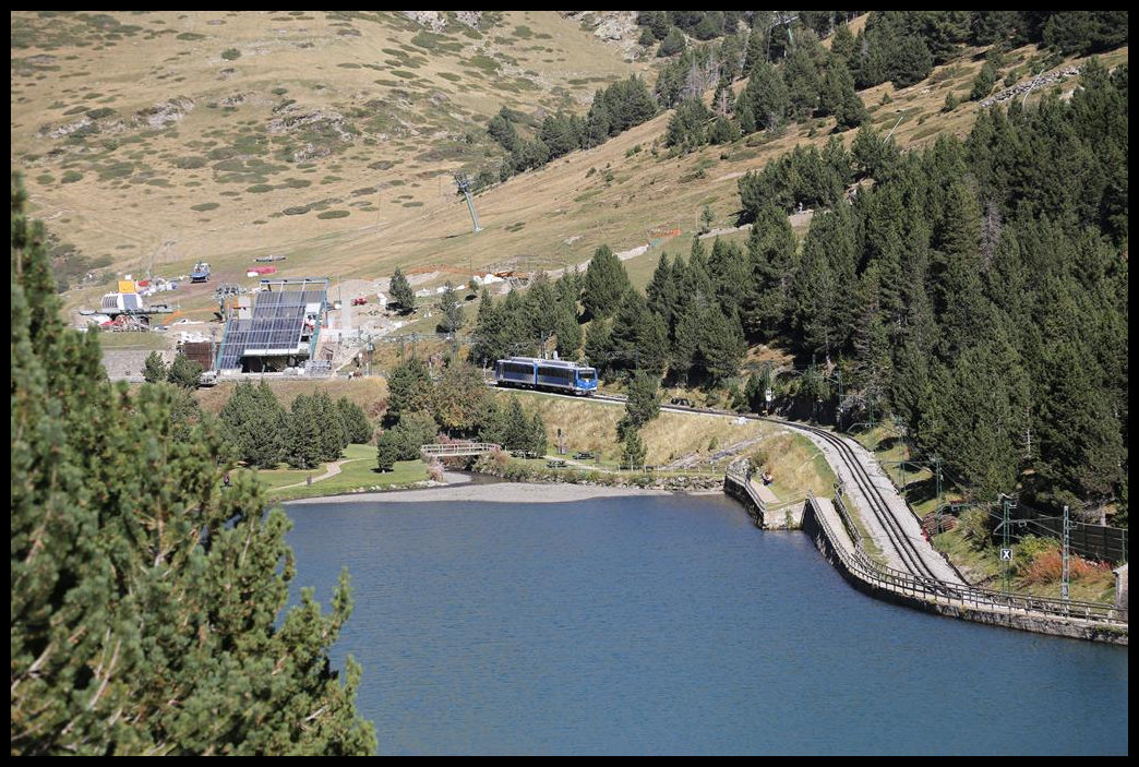 Blick auf den Stausee auf 1967 m Höhe in Núria. Dort ist die Endstation der Zahnradbahn von Ribes de Freser. Gerade verlässt hier am 11.10.2019, in Bildmitte zu sehen, der ET 6 den Bahnhof Núria und fährt ins Tal.
