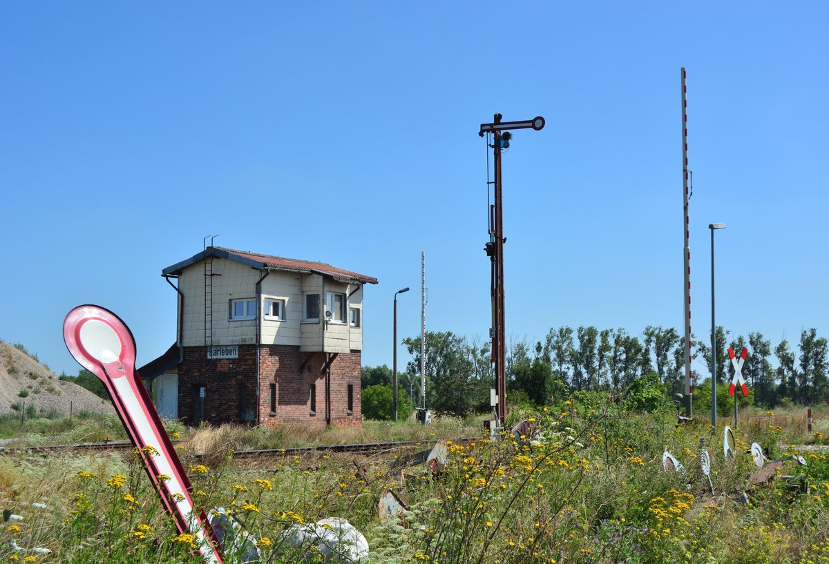 Blick auf das Stellwerk B1 in Barleben sowie das Ausfahrsignal Cäsar und den Bahnübergang. Im Vordergrund liegen 2 alte Formsignale die vor Jahren durch neue ersetzt wurden. 

Barleben 23.07.2019