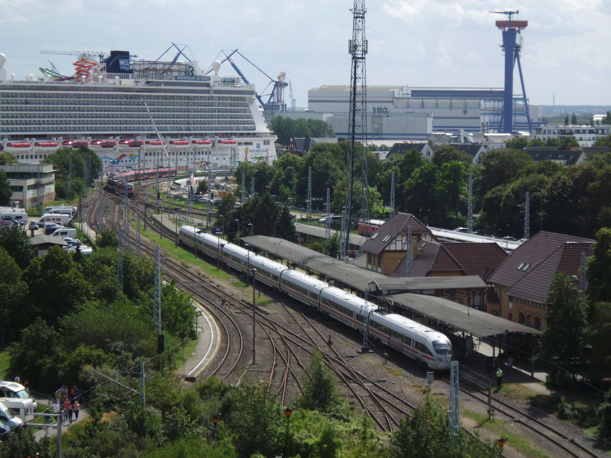 Blick auf den Warnemünder Hauptbahnhof: Im Vordergrund ein ICE Baureihe 411; hinten rechts die Warnow-Werft, hinten links das Kreuzfahrt-Schiff  Norwegian Gateway . Die Aufnahme entstand anläßlich der Hansesail 2019 am 11.8.2019- auf dem dortigen Jahrmarkt vom Riesenrad (!) aus.