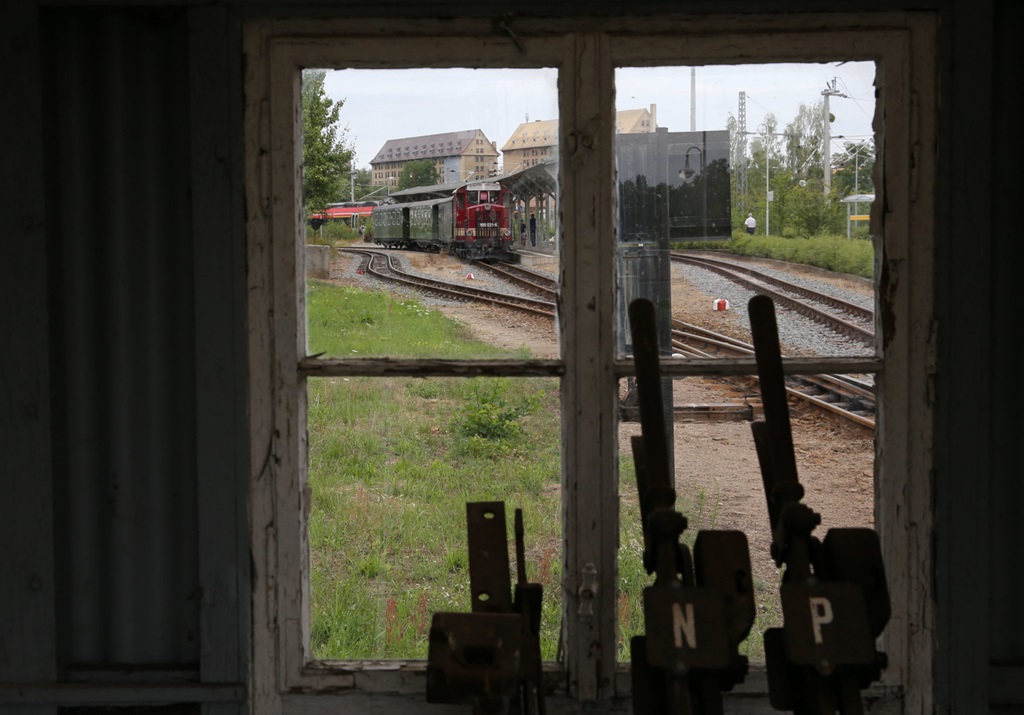 Blick aus dem still gelegten ehemaligen Stellwerk am Schmalspur Bahnhof Oschatz. Der Blick geht über die Stellhebel hinweg zum Bahnsteig. Dort steht gerade am 5.8.2023 um 10.40 Uhr der Zug 102 mit Lok 199031-6 nach Mügeln bereit.