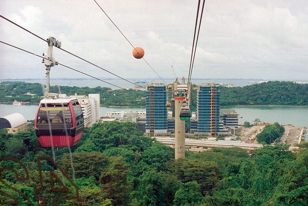 Blick aus der Gondel 42 der Singapore Cable Car MFLG Mount Faber-Linie auf weitere Gondeln, den ersten Stützturm, den Gebäudekomplex in dem sich im 16.Stockwerk die Harbour Front Station befindet, dem Keppel Harbour und die Insel Sentosa. Bild vom 08.Mai 2002. (Fotoscan)