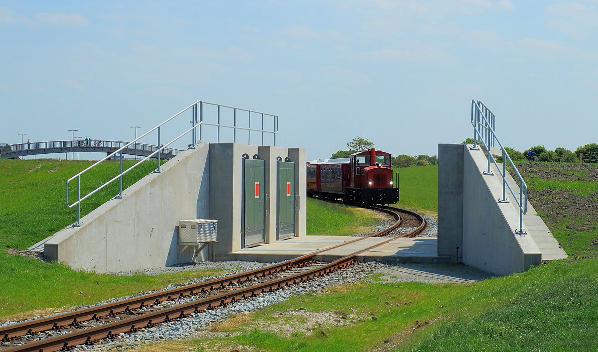 Blick durch das Deichtor auf Lok 4 der Langeooger Inselbahn, die am 02.06.2017 den Anleger in Richtung Ortsbahnhof verlässt