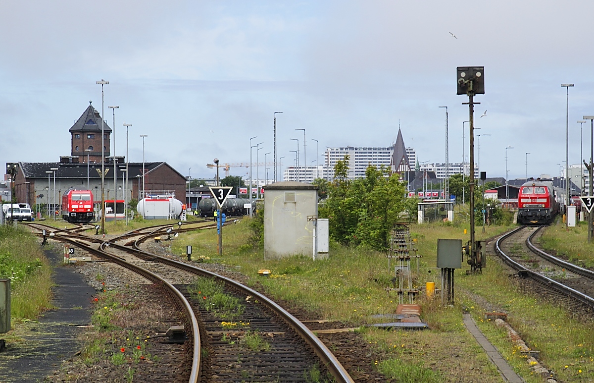 Blick vom (geöffneten) Bahnübergang der Straße Königskamp auf das Bw und den Wasserturm sowie die Autoverladung in Westerland mit 245 021 und 218 435-6 (07.06.2022)
