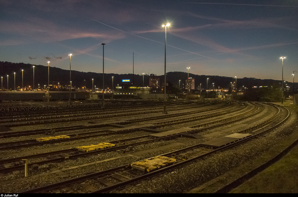 Blick von der Richtungsgruppe des Rangierbahnhofs Limmattal zurück in Richtung Ablaufberg. Unter dem IKEA-Leuchtschild ist das Stellwerkgebäude zu sehen. Im Vordergrund sieht man drei Rollwagen, von denen jedes Richtungsgleis einen besitzt und der Güterwagengruppen bis zu 500 Tonnen verschieben kann. Fotografiert an einer öffentlichen Führung am 2. Dezember 2016.