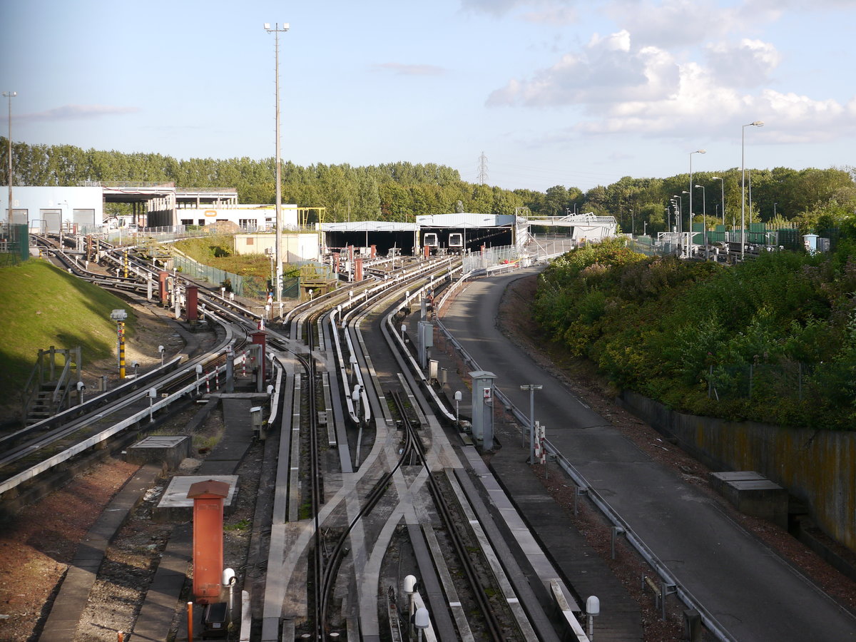 Blick zur Hauptwerkstätte Atelier de Quatre Cantons der Métro Lille mit zwei Zügen des  Typs VAL-208.
Hier in Villeneuve d'Ascq bei Lille nimmt die VAL-Strecke ihren Anfang und hier liegen auch die Anfänge des VAL-Systems.
Die Konzept einer leichten automatischen Métro wurde an der Universität Lille ab 1968 entwickelt.
Die erste konzipierte Strecke war: Villeneuve d'Ascq à Lille, abgekürzt VAL.
Nachdem das System dann erfolreich war, wurde VAL dann zum benannten Akronym für: Véhicule Automatique Léger (leichtes automatisches Fahrzeug).
Ab 1977 begann der Bau und 1983 wurde die Linie 1 der Métro Lille eröffnet.
2014-08-31  Villeneuve d'Ascq-Quatre-Canton
