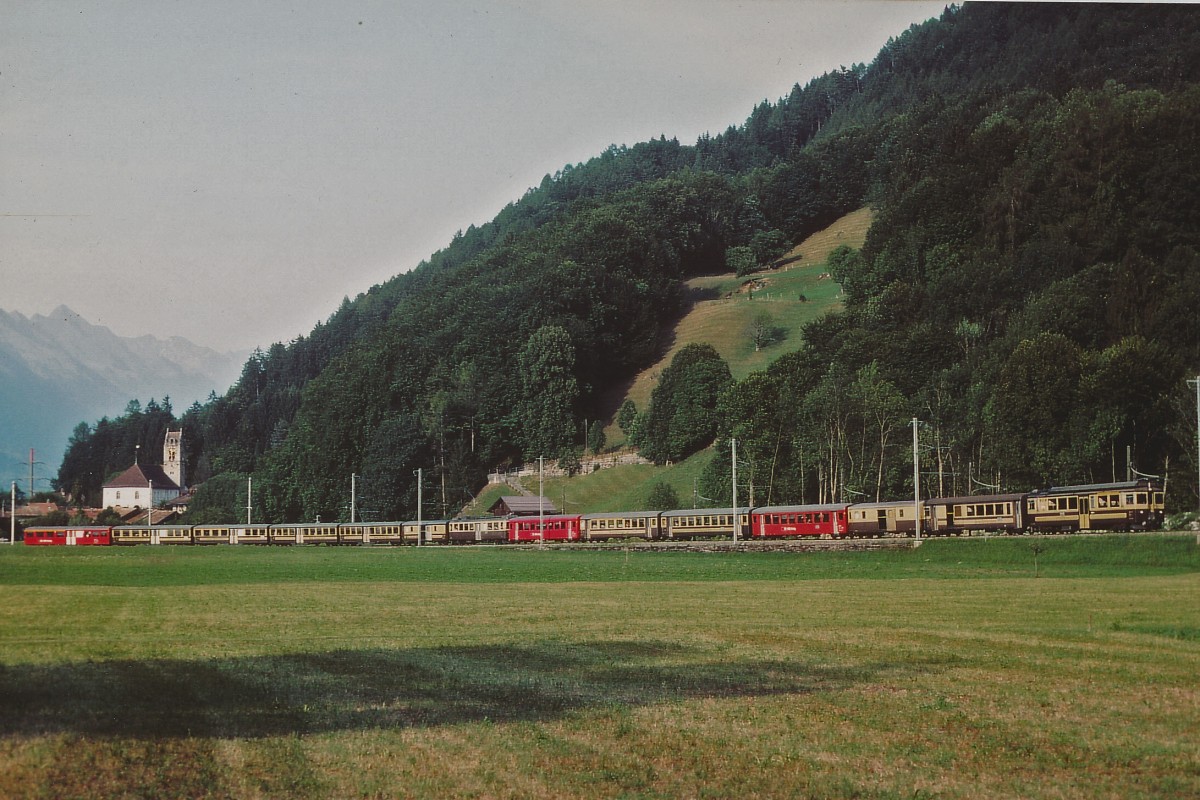 BOB: Vereinter 14-Wagen-Zug mit ABeh 4/4 II 311-313 (1986) und ABeh 4/4 l 304-310 (1965,1979) nach Lauterbrunnen und Grindelwald bei Wilderswil im August 2003. Seit dem Jahre 2003 hat sich bei der BOB einiges verändert. Nebst modernerem Rollmaterial, verpendelten Zügen wechselte auch der Farbanstrich. Besonders zu beachten gibt es  die vielen Wagen, die von der Brünigbahn übernommen wurden. Nebst den drei roten Wagen sind es die vier bereits braunen Mitteleinstiegwagen.
Foto: Walter Ruetsch  