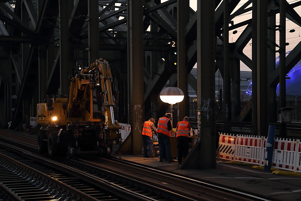  Brückenbild mit Stehlampe  oder  Produktionsberatung ! ;-) Am Abend des 13.03.2014 sind die Bauarbeiter auf der Hohenzollernbrücke in Köln gerade mit einer Besprechung, im Rahmen der zurzeit stattfindenden Sanierung der beiden südlichen Gleise des bekannten Bauwerkes, beschäftigt. Eine Baulampe erleuchtet die Szene. Um die Triebfahrzeugführer nicht zu blenden, ist diese im oberen Bereich abgedunkelt.