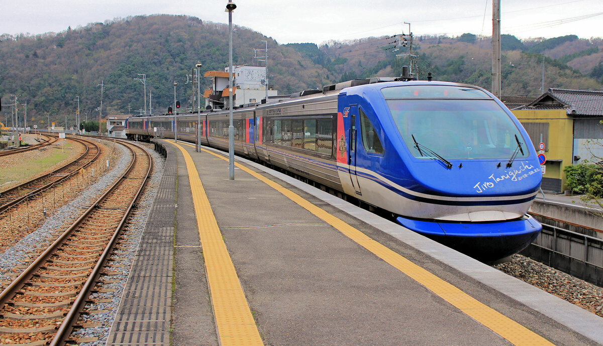 Chizu Kyûkô Privatbahn: Diese Bahn führt komfortable Expresszüge quer über den westlichen Zipfel der japanischen Hauptinsel Honshû und verbindet damit den Raum um die Stadt Tottori am Japanischen Meer mit den grossen Agglomerationen des Kansai-Gebiets, Kôbe, Ôsaka und Kyôto. Die ganze Reise dauert rund 4 Stunden. Die Chizu Kyûkô besitzt 34 Dieseltriebwagen Serie HOT 7000 mit neigbarem Wagenkasten aus den Jahren 1994-2002, die zu 5- oder 6-Wagenzügen zusammengestellt werden; alle Wagen eines Zugs sind angetrieben. Von den 34 Wagen haben 10 ein Panorama-Ende ohne Durchgang, 3 sind Frontwagen mit Durchgangstüre. Die Bezeichnung HOT verweist auf die 3 durchfahrenen Praefekturen, Hyôgo – Okayama – Tottori. Im Bild ein 5-Wagenzug mit dem Frontwagen HOT 7004 namens «Taniguchi Jirô», benannt nach einem bekannten Manga-Zeichner aus Tottori (1947-2017). Im Bahnhof Sayo, 7.April 2015 