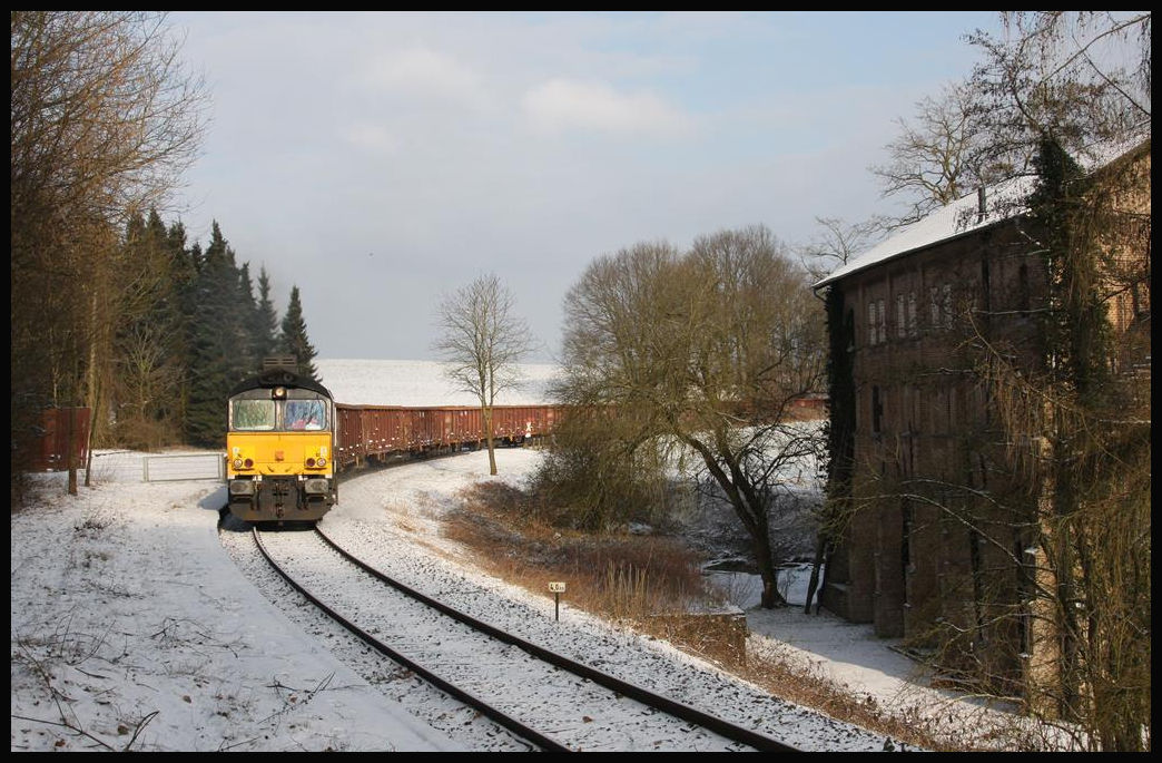 Class 66 8653-01 im ehemaligen Haltepunkt Augustaschacht. Hier ist sie am 24.2.2018 mit einem Schrottzug zur Georgsmarienhütte unterwegs. Hinter dem Zaun links von der Lok stand früher das Bahnhofsgebäude, eine Holzbaracke mit Fahrkartenverkauf und Wartehalle.
Rechts ist das Gebäude der Gedenkstätte Augustaschacht zu sehen, welches früher Teil eines Arbeitszuchtlagers war. Ursprünglich war es auch das Pumpenhaus für die Tagebauten am Hüggel. Eine riesige Dampfpumpe sorgte für die Trockenlegung der Erzlagerstätten oberhalb von Hasbergen.
