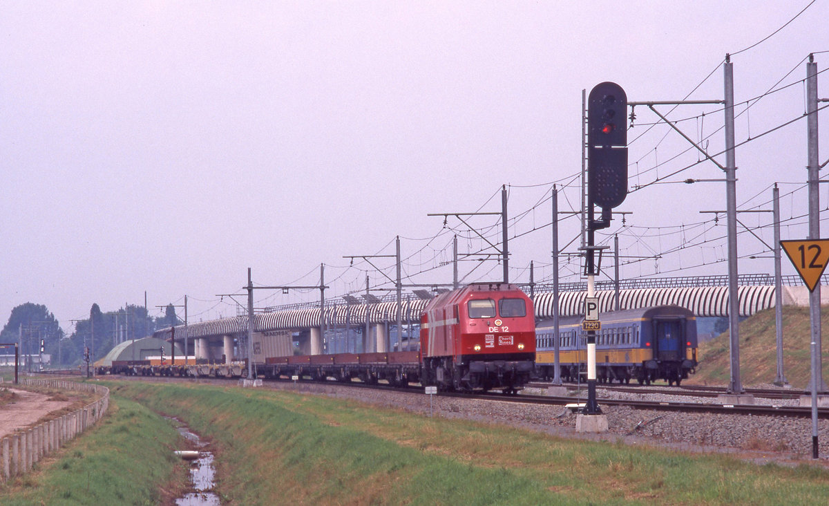 Containerzug der Firma Shortlines auf dem Weg von Europoort nach Sittard. Es führt Lok DE12 der HGK als Zug Nr.98101, hier bei Boxtel am 01.08.1998.
In der Anfangszeit dieser neuen Gesellschaft war die Auslastung der Züge ziemlich mässig, wie man sieht. 
Bemerkenswert ist auch das Hauptsignal Nr.1230, das in Fahrtrichtung links plaziert wurde, was in den Niederlanden nicht sehr oft vorkommt. Wie in Deutschland werden Signale links plaziert wenn rechts der Platz dazu fehlt.
Scan vom Dia (Fujichrome).