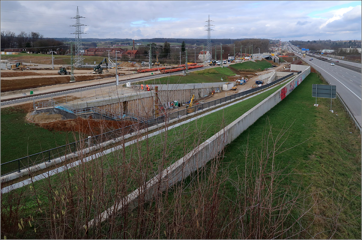 Da wo sich - 

... Stuttgart 21 und die NBS nach Ulm die Hand geben: Wendlingen. 

Die Schnellfahrstrecke nach Stuttgart verläuft parallel zur Autobahn A8. Bis zu den zwei Güterwagen oben in Bildmitte liegen schon die Gleise. 
Links oben an dem Raupen-Baufahrzeuge beginnt der Trog zum Tunnel der kleinen Wendlinger Kurve, wo später die Züge aus Richtung Stuttgart nach Tübingen abbiegen.
Die Bauarbeiter links der Bildmitte stehen über dem Tunnelportal der großen Wendlinger Kurve auf der die Züge. Hier werden die Züge aus Tübingen auf die Neubaustrecke zum Flughafen und nach Stuttgart geleitet. Dabei wird auch die oben weiter rechts zu sehende schräg zu den Hauptgleisen liegende Brücke befahren. 
Hinter dem diagonal durch das Bild laufende Gelände liegt in einem Trog das Gleis der Güterzuganbindung. Über dieses werden später Güterzüge aus/in Richtung Plochingen auf die Neubaustrecke geleitet. 
Ab Dezember 2022 werden über diese Verbindungsgleis die Fernverkehrszüge die dann in Betrieb gehende Neubaustrecke von Wendlingen bis Ulm auf die neue Strecke geleitet.

Foto von einem Fuß und Radweg.

04.02.2022 (M)
