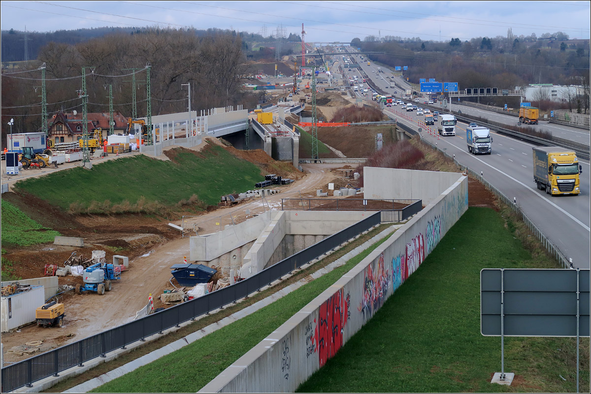 Da wo sich - 

... Stuttgart 21 und die NBS nach Ulm die Hand geben: Wendlingen. 

Die Brücken links der Bildmitte links der Bildmitte führen über die vorhandene Bahnstrecke Plochingen - Tübingen. Die schräge liegende Brücke ist Teil der großen Wendlingen Kurve. Dahinter folgt die Brücke über den Neckar und dann der Anstieg zur Filderhöhe parallel zur Autobahn.
Im Vordergrund unten ist der Trog der Güterzuganbindung zu sehen. Diese Gleis unterfährt in einem bergmännisch gebauten kurzen Tunnel die Autobahn und mündet dann in die Bahnstrecke Richtung Plochingen ein. Von Dezember 2022 bis voraussichtlich 2025 wird der gesamte Verkehr der Neubaustrecke über diese Gleis geführt werden. Dann soll mit Stuttgart 21 der Rest der Schnellfahrstrecke in Betrieb gehen.

Foto von einem Fuß und Radweg.

04.02.2022 (M)