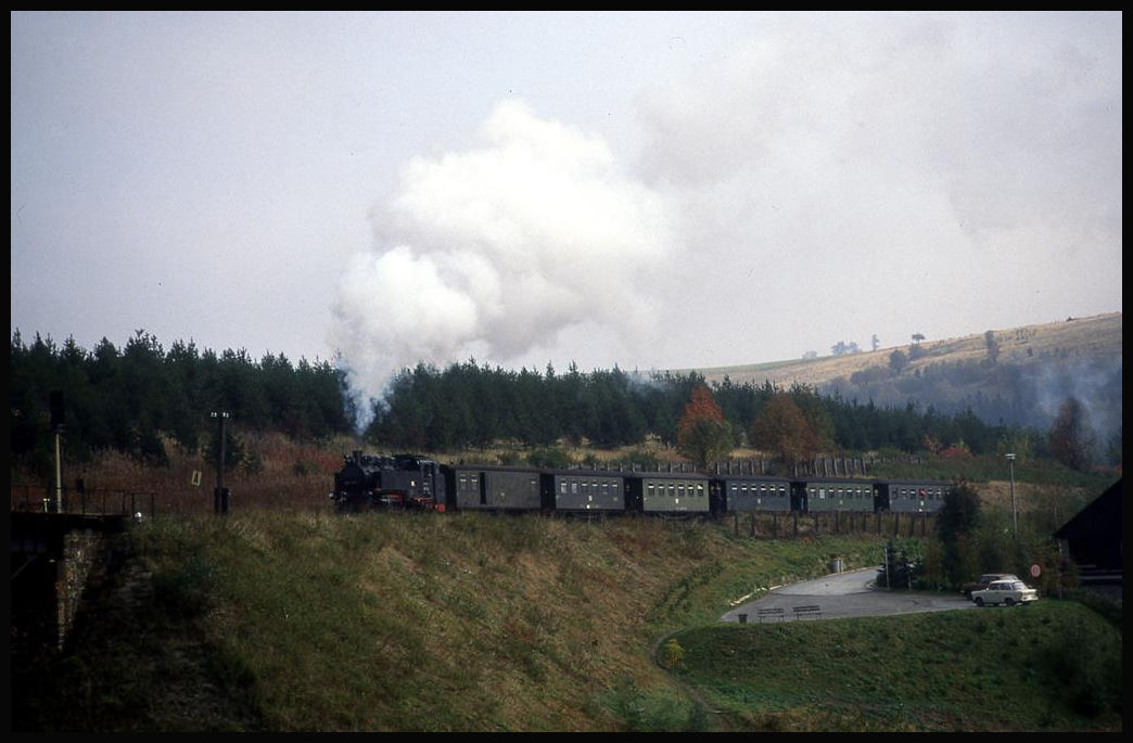 Dampflok 99740 befindet sich hier am 8.10.1992 um 11.15 Uhr in Anfahrt auf das Viadukt in Oberwiesenthal. Zu diesem Zeitpunkt gehörte die Relikte, wie Trabbi und Wartburg, noch zum täglichen Erscheinungsbild, was man unschwer auf dem kleinen Parkplatz rechts vor dem Zug erkennen kann!