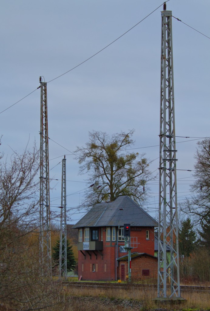 Das ehemalige Weichenwärter Stellwerk (Außerbetriebnahme 18.03.2005) in Ducherow zwischen Oberleitungsmasten gesehen. - 22.12.2013