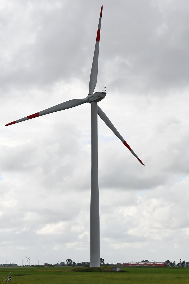 Das überdimensionale Windrad lässt den vorbeifahrenden Regionalexpress nahezu verschwinden. Als Größenvergleich finde ich das Bild aber trotzdem ganz interessant. (bei Niebüll, Juni 2024)