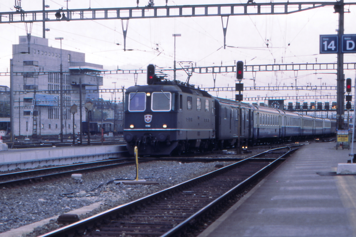 Das Zentralstellwerk von Zürich HB war im Jahr 1987 noch das markanteste Bauwerk in der Umgebung. Gerade fährt die Re 4/4 II der SBB mit einem Schnellzug nach Brig auf Gleis 13 in Zürich HB ein. Hinter dem Gepäckwagen laufen EW II der BLS - als  Naturalausgleich  für geleistete Kilometer von SBB-Waggons auf BLS-Gleisen. Der Zug hatte damals eine gewisse Bekanntheit unter Eisenbahnfreunden und in der einschlägigen Presse. Mittlerweile haben die SBB den Fernverkehr der BLS übernommen und dafür den Regionalverkehr im Kanton Bern an die BLS abgetreten - für solch bunte Züge gibt es keinen Grund mehr.
Zürich HB, 24. August 1987; Canon AE1, Canoscan, Gimp