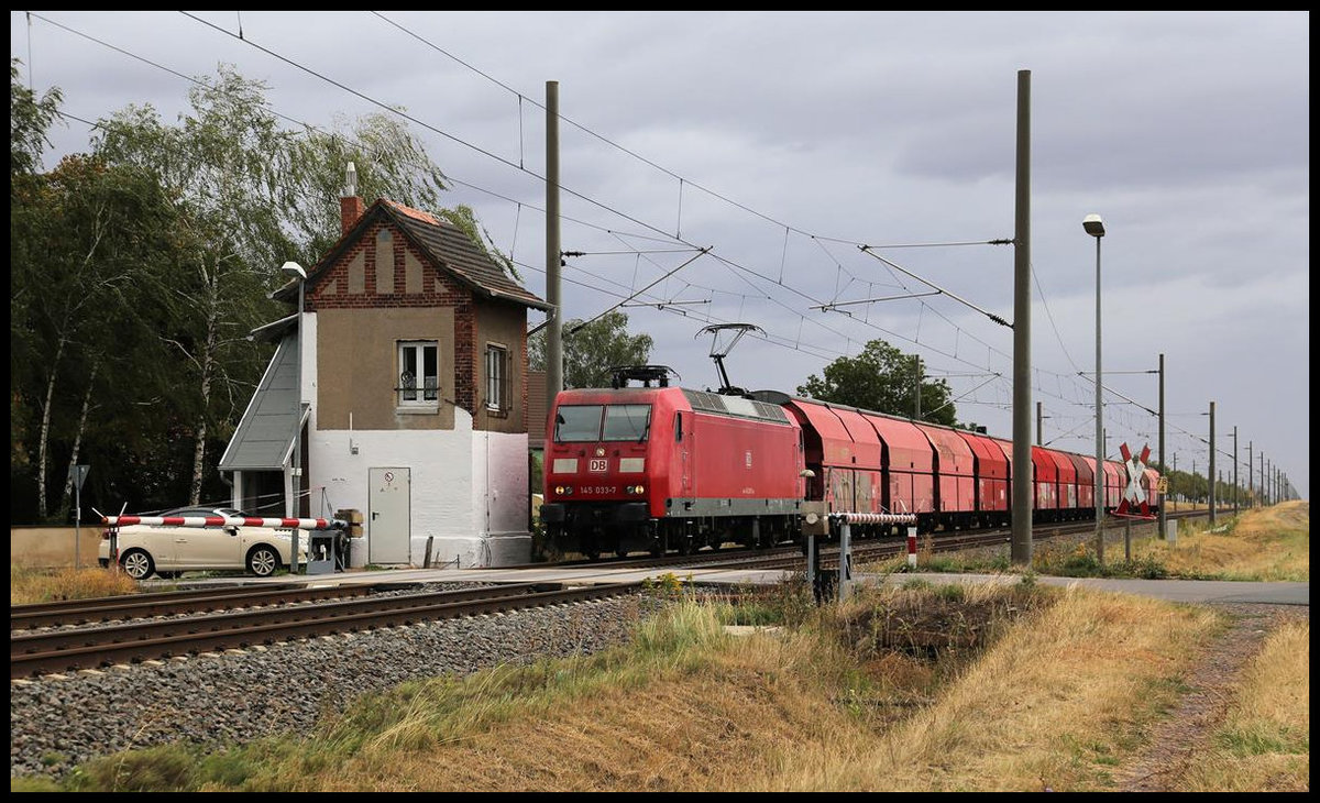 DB 145033-7 passiert hier am 26.8.2020 um 11.06 Uhr mit einem Ganzzug in Richtung Halle den Schrankenposten bei Braschwitz.