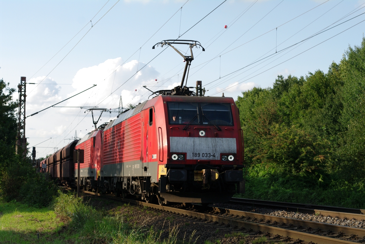 DB 189 033-4 und 030-0 fahren am 28.08.2015 in Ratingen-Lintorf ihren Erzzug erneut an, nachdem sie an einem kleinen Bahnübergang mit Schrankenstörung einen full-stop einlegen mussten. Die Lokomotiven und die Wagen sind mit automatischen C-AKv-Kupplungen ausgestattet.