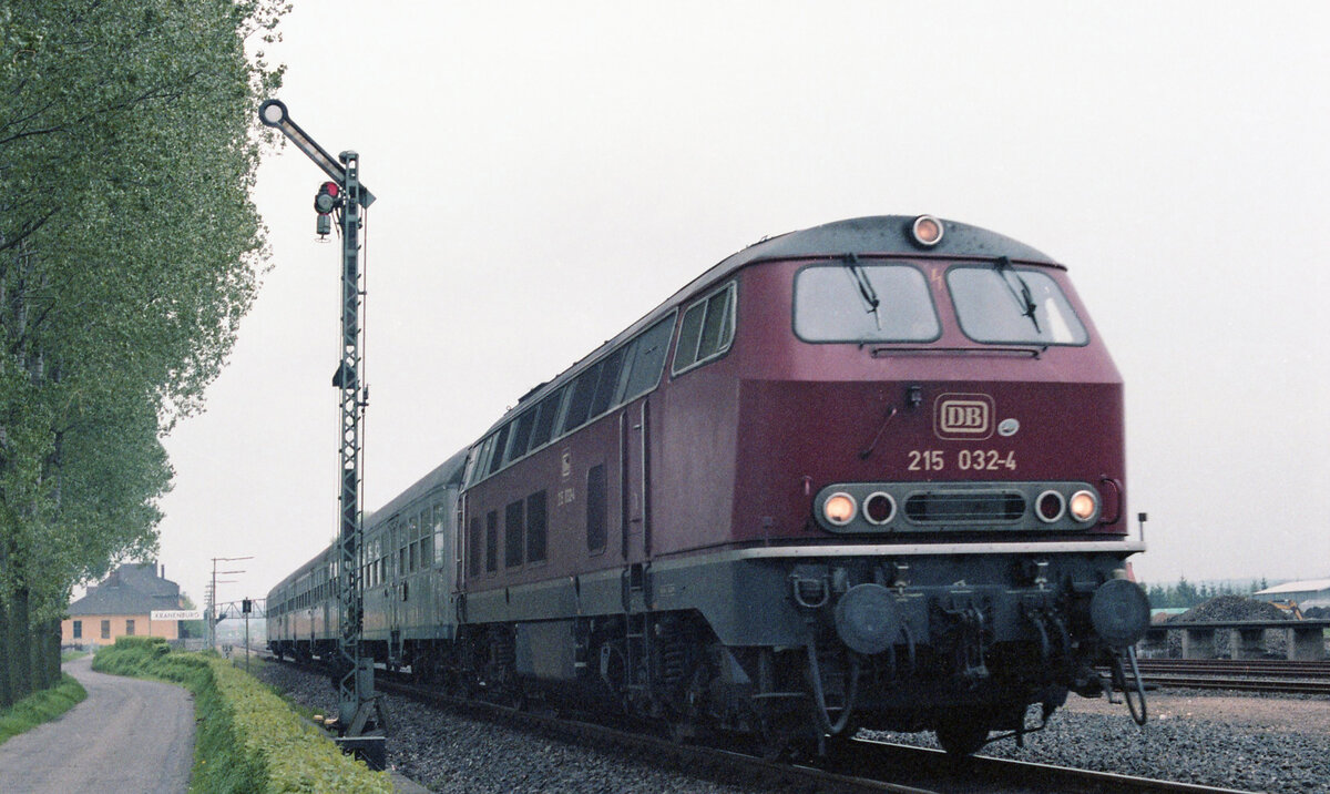 DB 215 032-4 mit E-3778 (Siegen - Nijmegen) bei der Abfahrt vom Gleis 1 in Kranenburg am 15.05.1983. Der Zug passiert gerade Formsignal  H , das noch Propangasleuchten hat. Scanbild 93075, Kodacolor400.