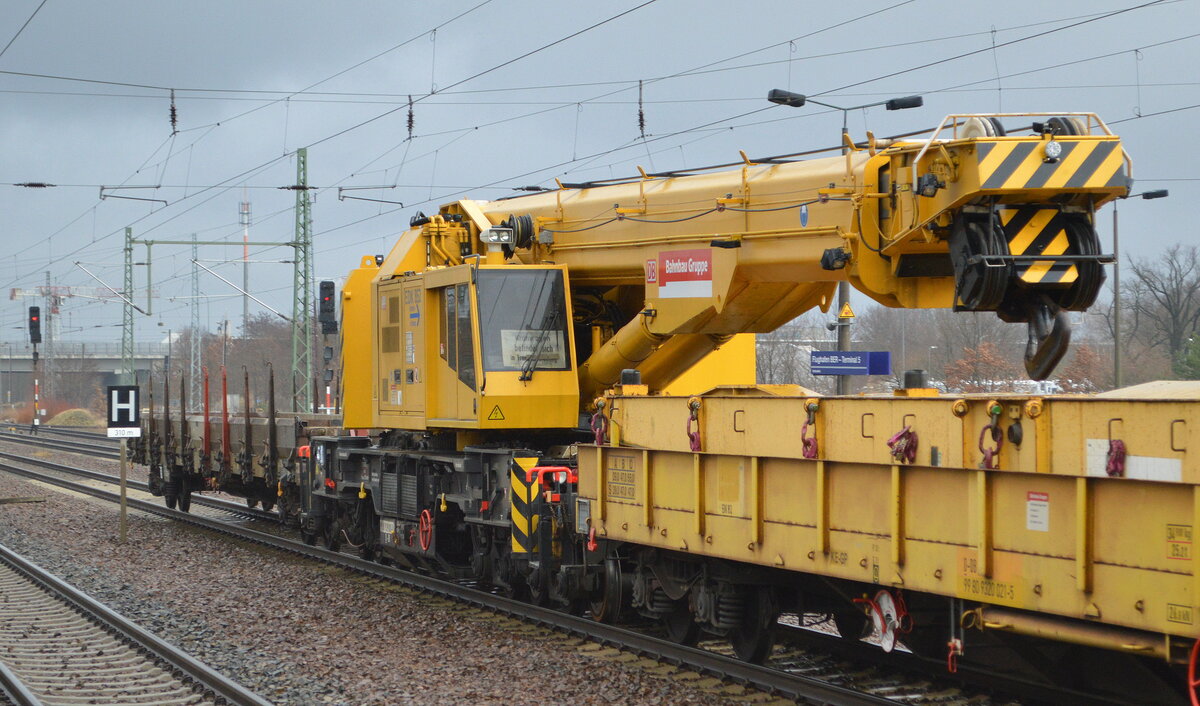 DB Bahnbau Gruppe mit dem Gleisbauschienenkran KRC 810 T (EDK 852, Baujahr 2002) mit der Nr.  99 80 9319 001-0 D-DB  am Haken von  232 550-4  am 26.01.22 bei der Durchfahrt Bf. Flughafen BER - Terminal 5.