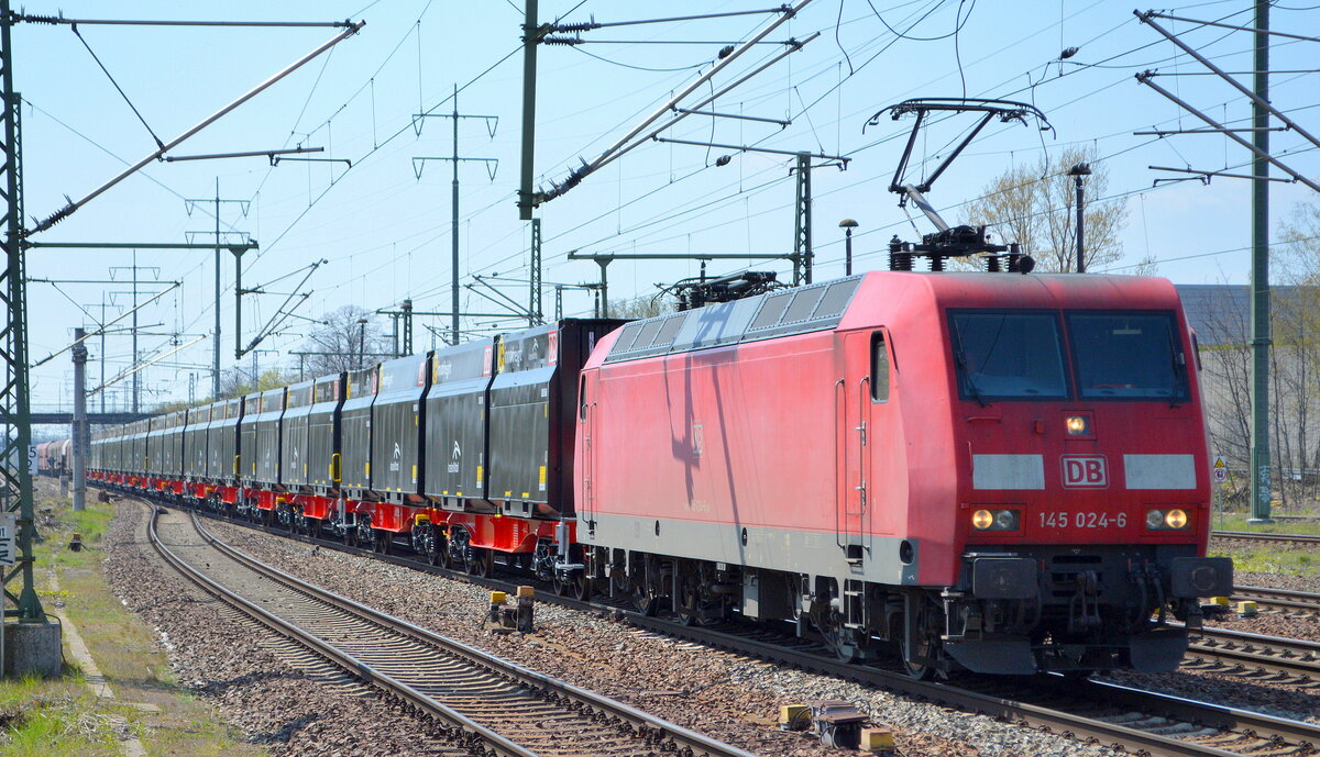 DB Cargo AG [D] mit  145 024-6  [NVR-Nummer: 91 80 6145 024-6 D-DB] und den neuen Schüttgutcontainerwagen für Koks für das EKO Stahlwerk von ArcelorMittal der Wagengattung Sggmrrs 701 mit schwarzen innofreight Containern am 28.04.21 Durchfahrt Bf. Flughafen BER Terminal 5. 